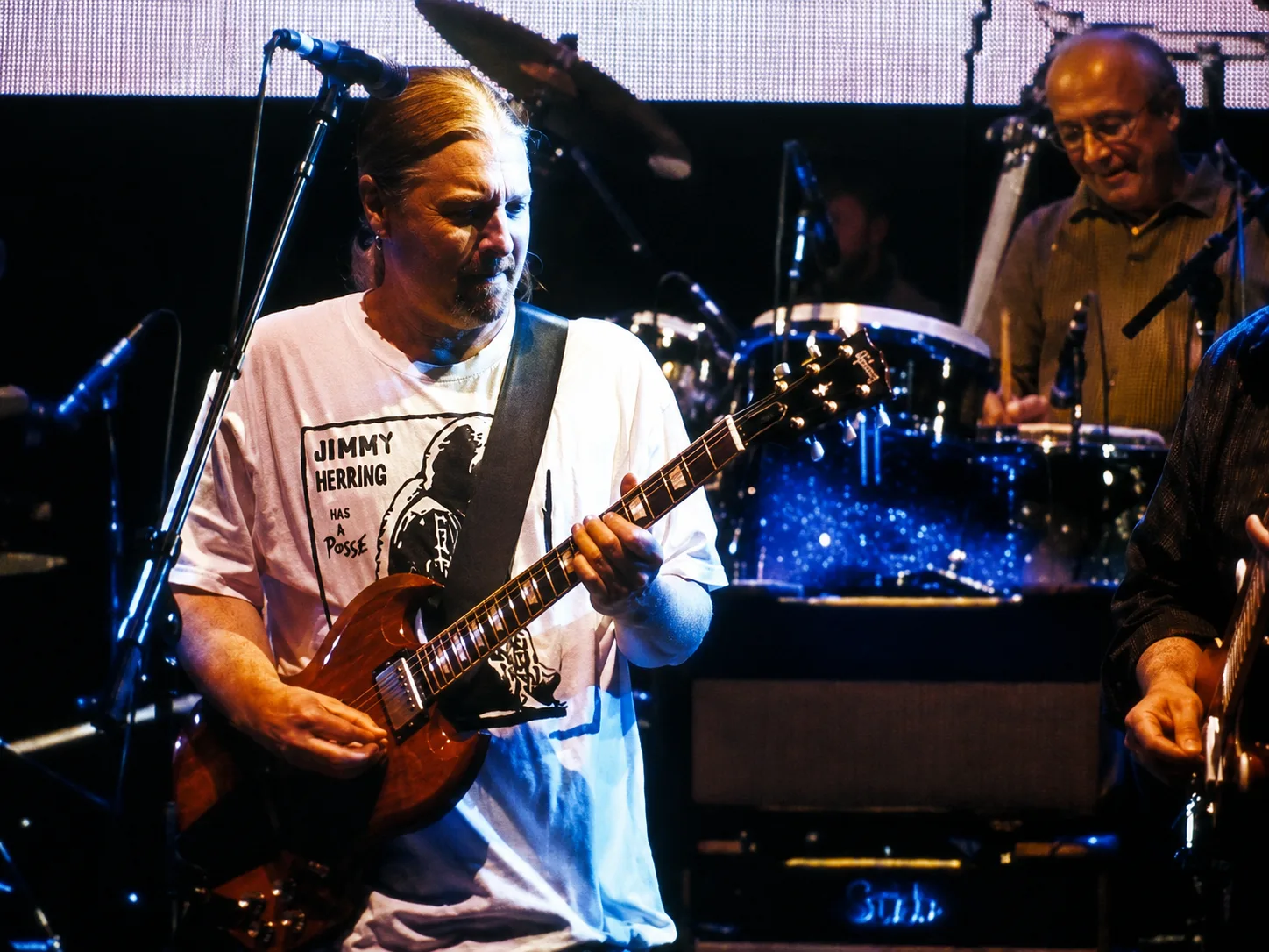 Derek Trucks onstage in a Jimmy Herring Has a Posse shirt